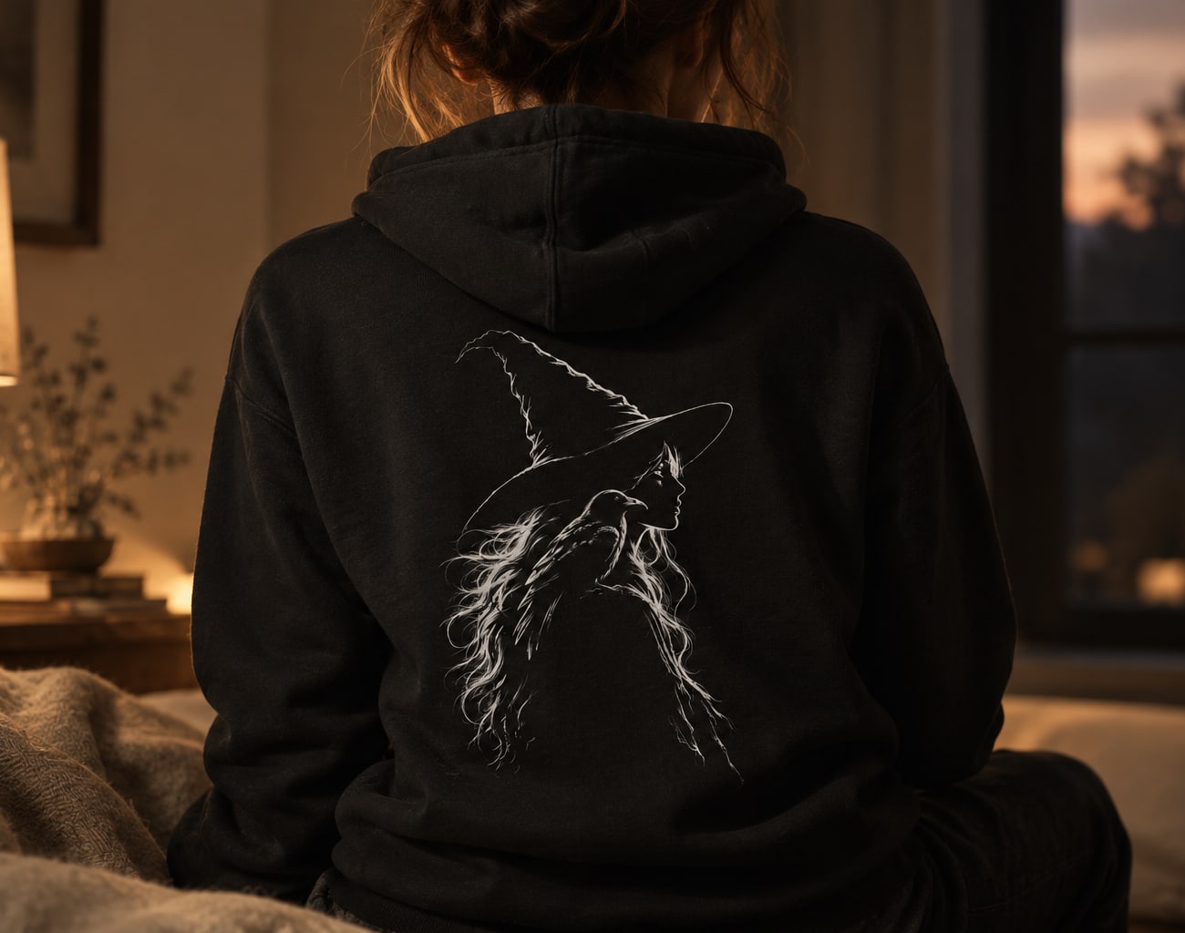 The back of a black hoodie printed with a witch and crow drawn only in edge light